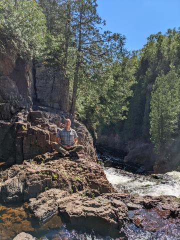 Matthew meditating on a rock near a river