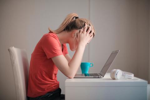 woman sitting at a laptop with her hands on her head staring at a screen