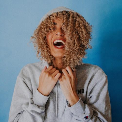 Someone with long curly blonde hair and a hoodie laughing