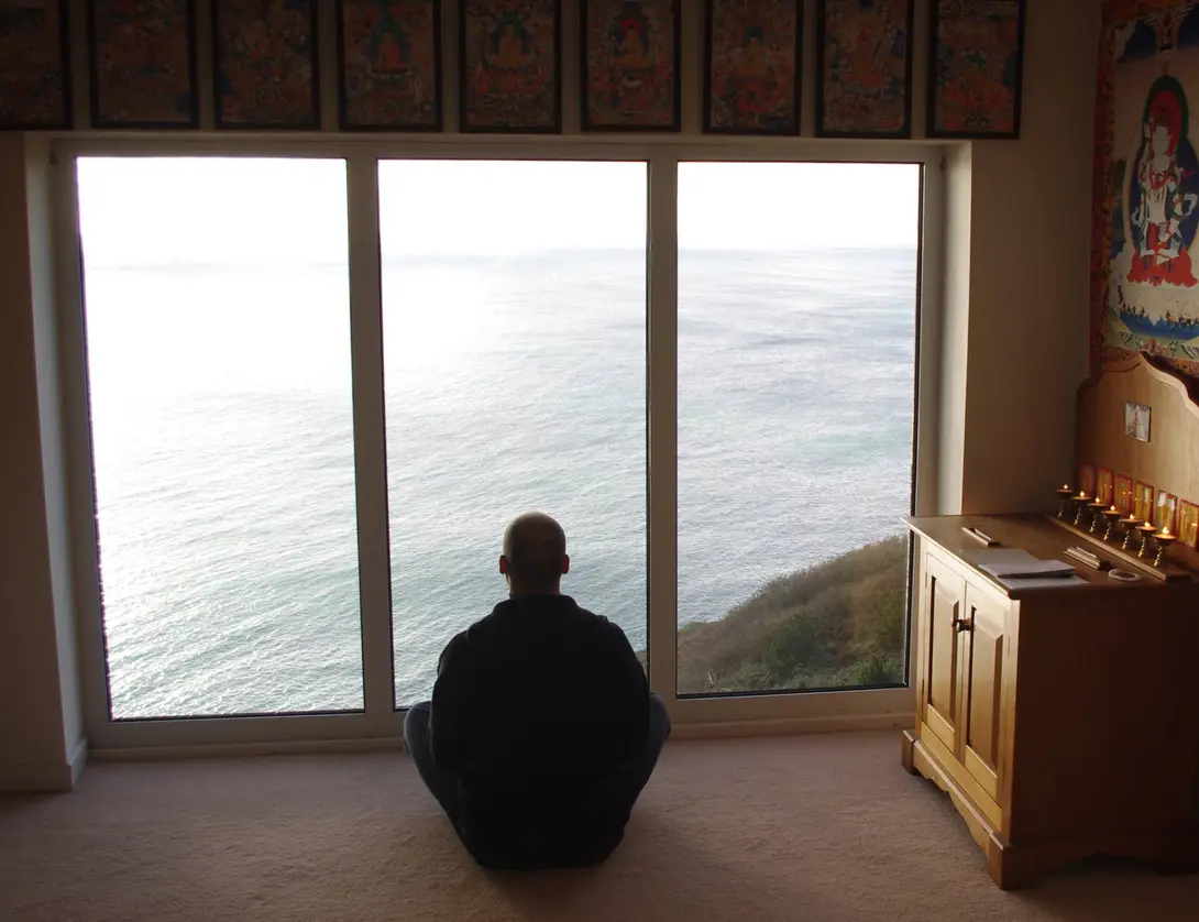 Matthew sitting in a room with a large window at a Buddhist retreat center overlooking the cliffs of Ireland