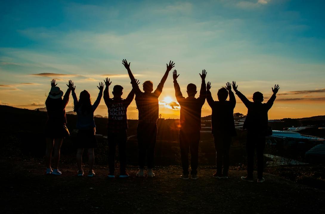 people standing outside at sunset with their arms raised